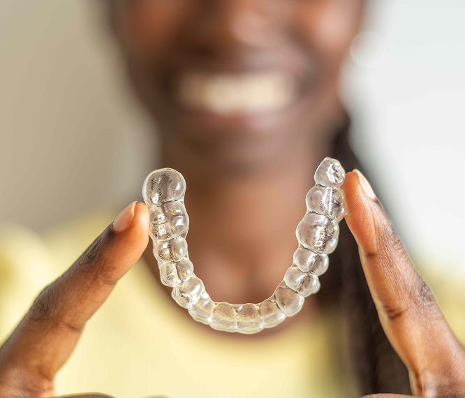 A Dark Skinned Figure Holding Clear Aligners To The Foreground