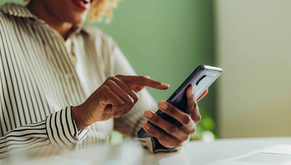 Dark Skinned Woman Using Her Phone At A Table Wearing A Striped Shirt