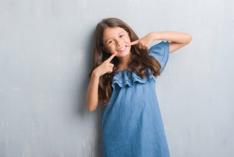 Young hispanic kid over grunge grey wall smiling confident showing and pointing with fingers teeth and mouth. Health concept.