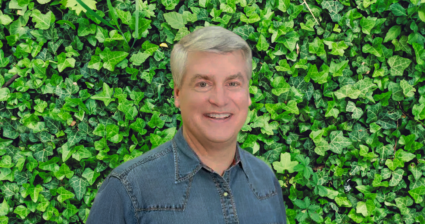 Dr Bill Lange standing in front of green ivy wall.